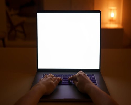 Hands typing on a laptop with dimmed screen in a low light room